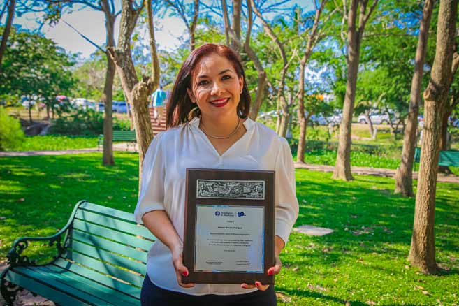 Adriana Morales sosteniendo su reconocimiento como profesora inspiradora