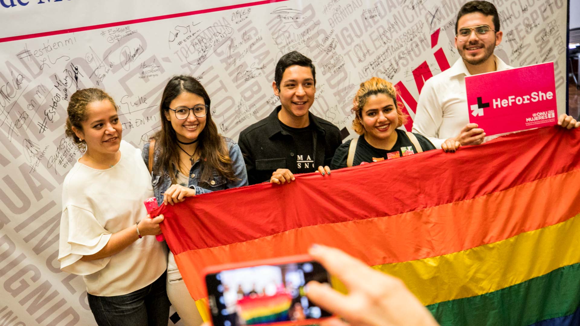 Jovenes con bandera LGBTI y pancartas de HeForShe