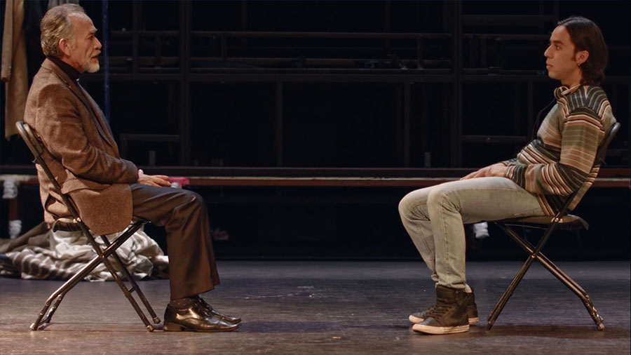 Dos actores en un escenario sentados frente a frente