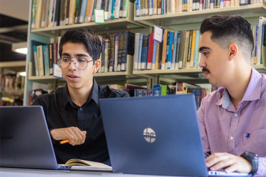 Dos estudiantes redactando su paper en biblioteca