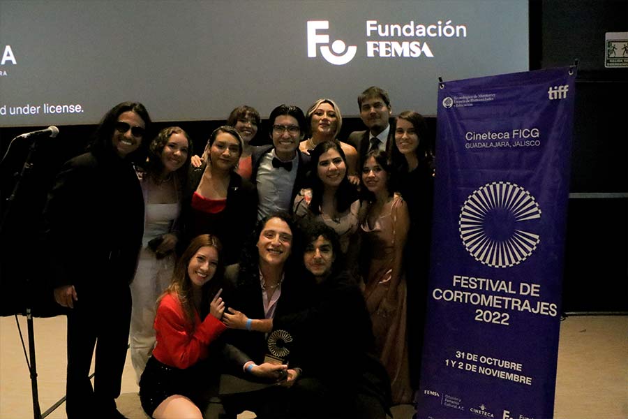 Estudiantes realizadores del cortometraje La Magia posan con su premio frente al cartel del festival