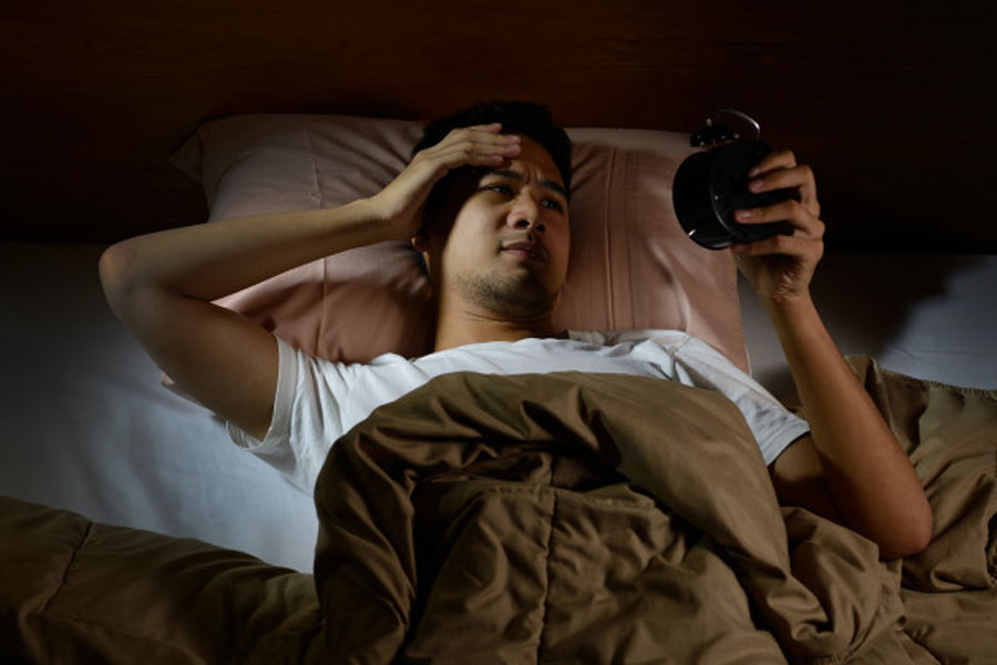 Hombre deprimido que sufre insomnio mirando despertador acostado en la cama
