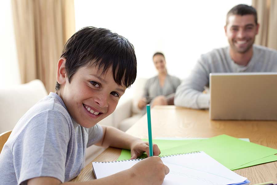 Niño sonríe al realizar actividades en casa, mientras sus papás realizan home office