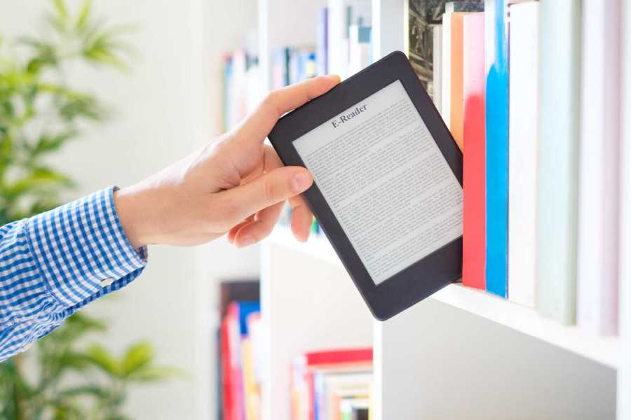 Librero con libros tradicionales, mientras una persona elige del librero un dispositivo de lectura digital