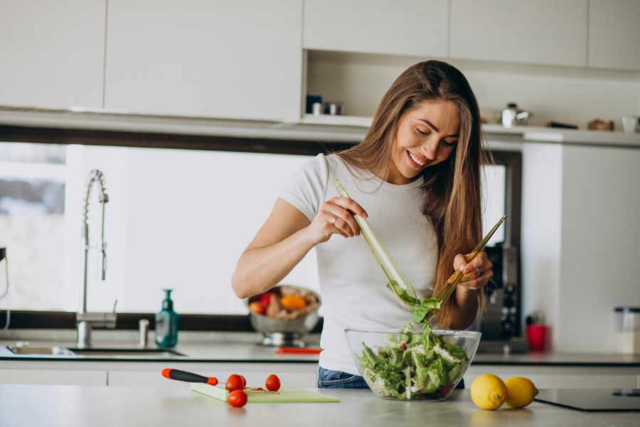 Mujer en la cocina preparando su ensalada con diversas verduras.