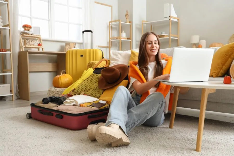 Mujer joven trabajando en su laptop con maleta de viaje a medio llenar