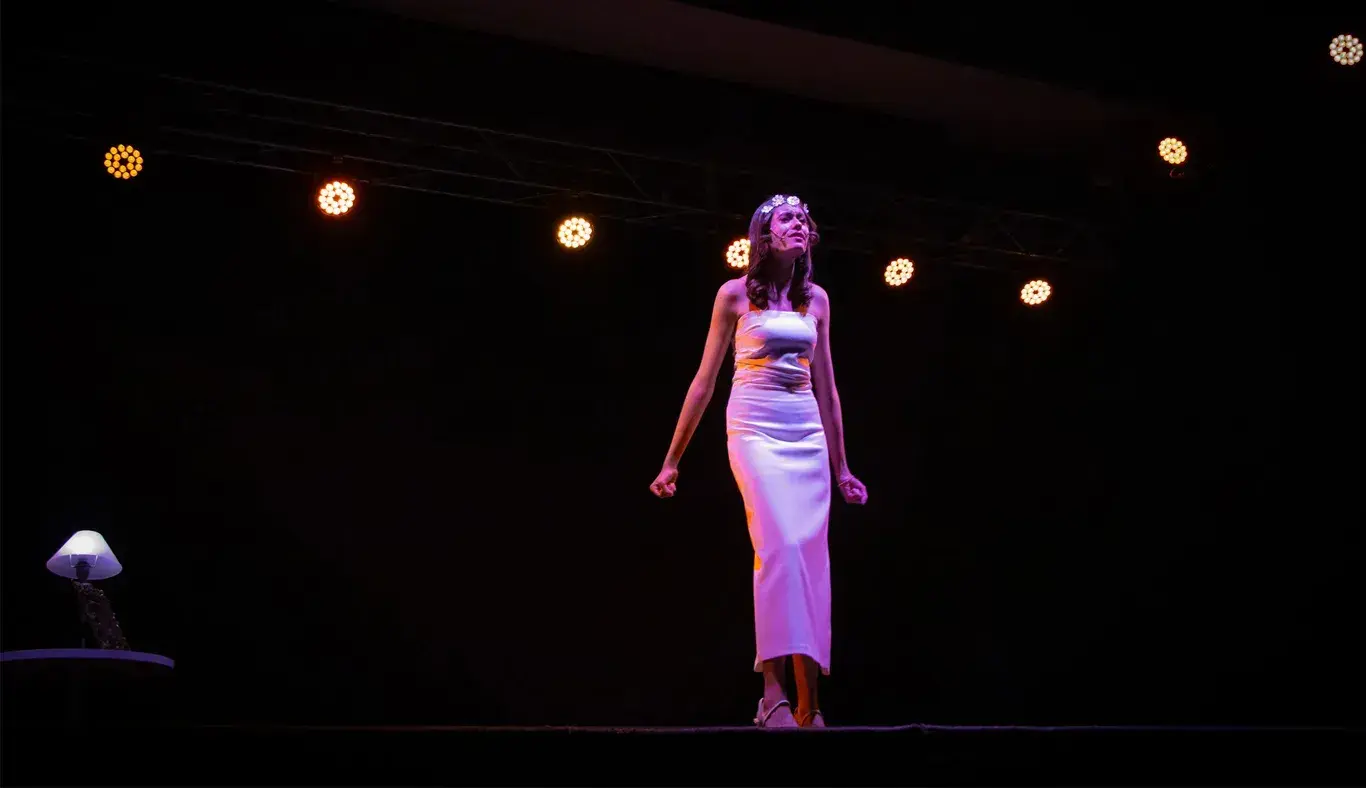 Miembro del representativo de teatro usando un vestido blanco a medio monólogo