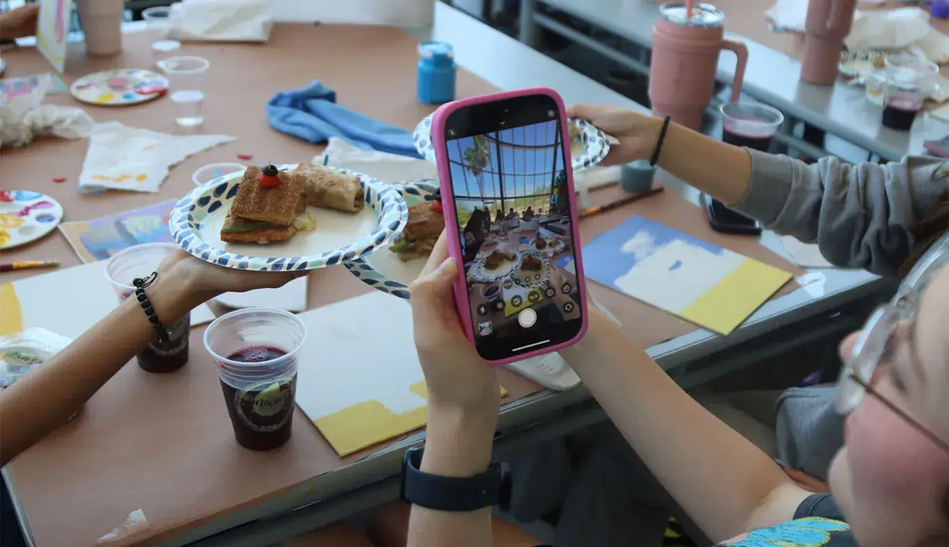 Chica tomando una foto con su celular de una mesa cubierta con comida y lienzos.