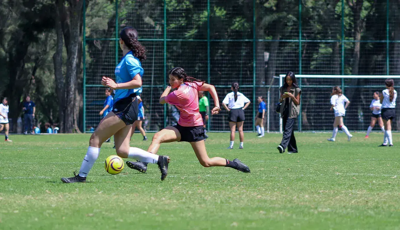 Jugadora de fútbol corre mientras patea el balon. 