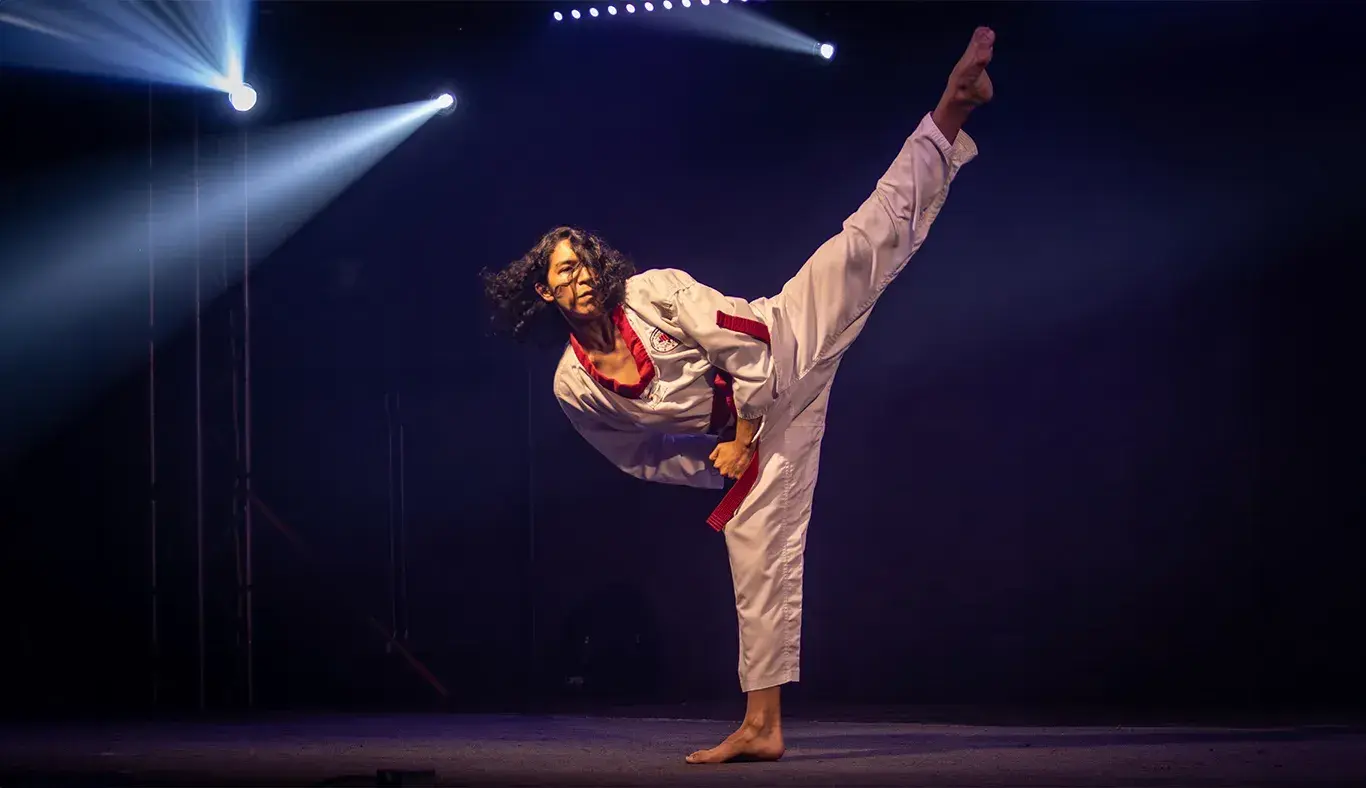 Rod Mendoza, karateka, ejecutando una patada alta con equilibrio durante su presentación en Tec's Got Talent en un escenario iluminado.