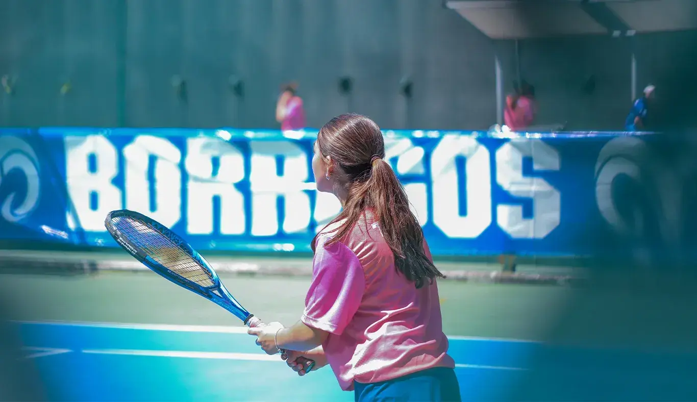 Alumna de espaldas sosteniendo raqueta de tenis. 