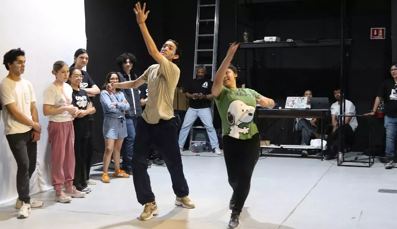 Dos jóvenes actuando en medio de un grupo de actores. 