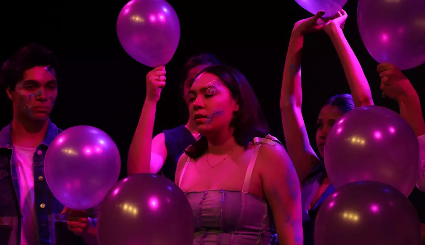 Chica en escena rodeada de personas sosteniendo globos. 
