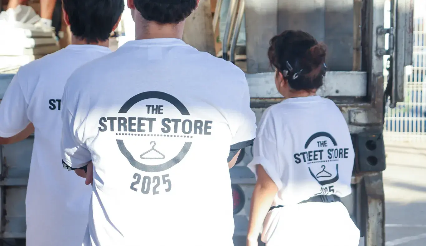 Vista de espaldas de tres voluntarios portando camisetas blancas con un logo que dice Street Store 2025.