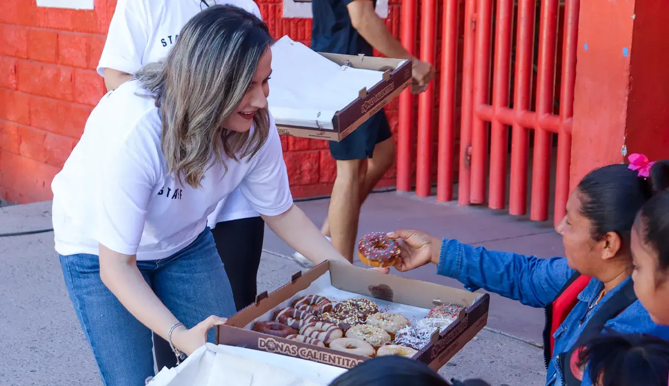 Mujer repartiendo donas a personas sentadas en sillas. 