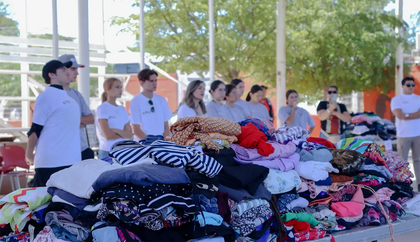 Mesas con ropa doblada y apilada con personas formadas en el fondo. 