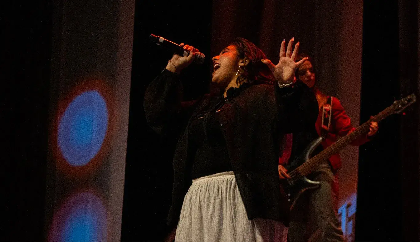 Chica cantando en escenario con top negro y falda blanca.