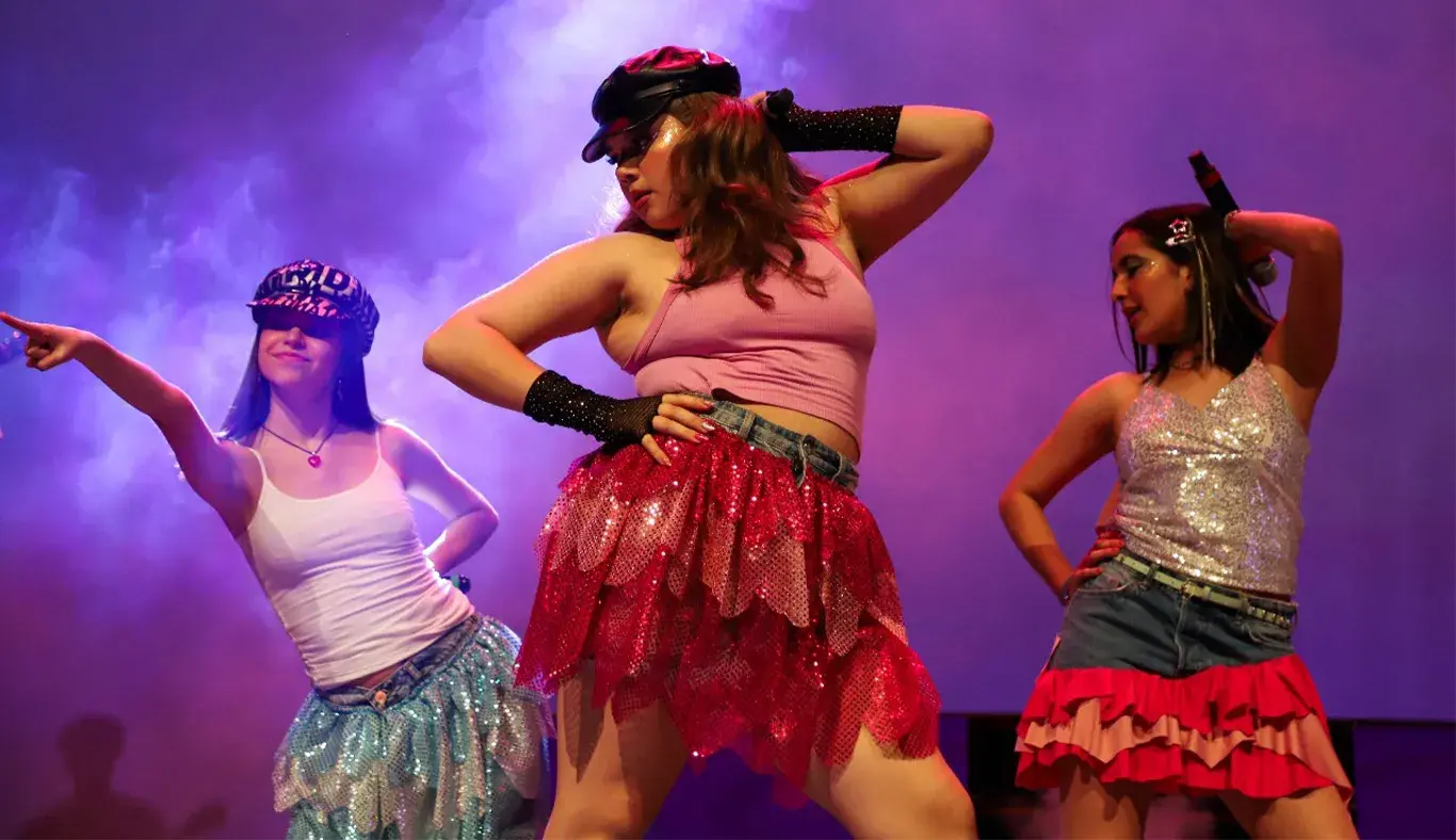 Tres jóvenes adolescentes en escenario con ropa al estilo de la moda de los 2000.