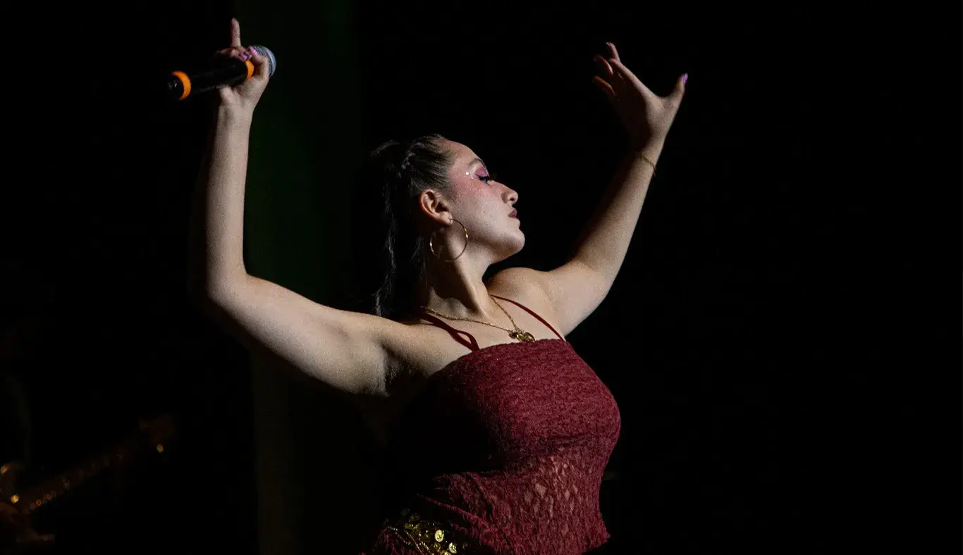 Mujer vestida de rojo sosteniendo ambos brazos en el aire en posición de belly dance. 