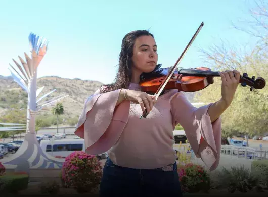 Mariana Páez tocando la viola frente a una vista de la Cápsula del Tiempo del campus Sonora Norte