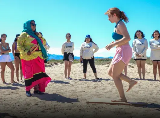 Adolescente hace baile tradicional guiada por un miembro de la comunidad Comca'ac en la playa.