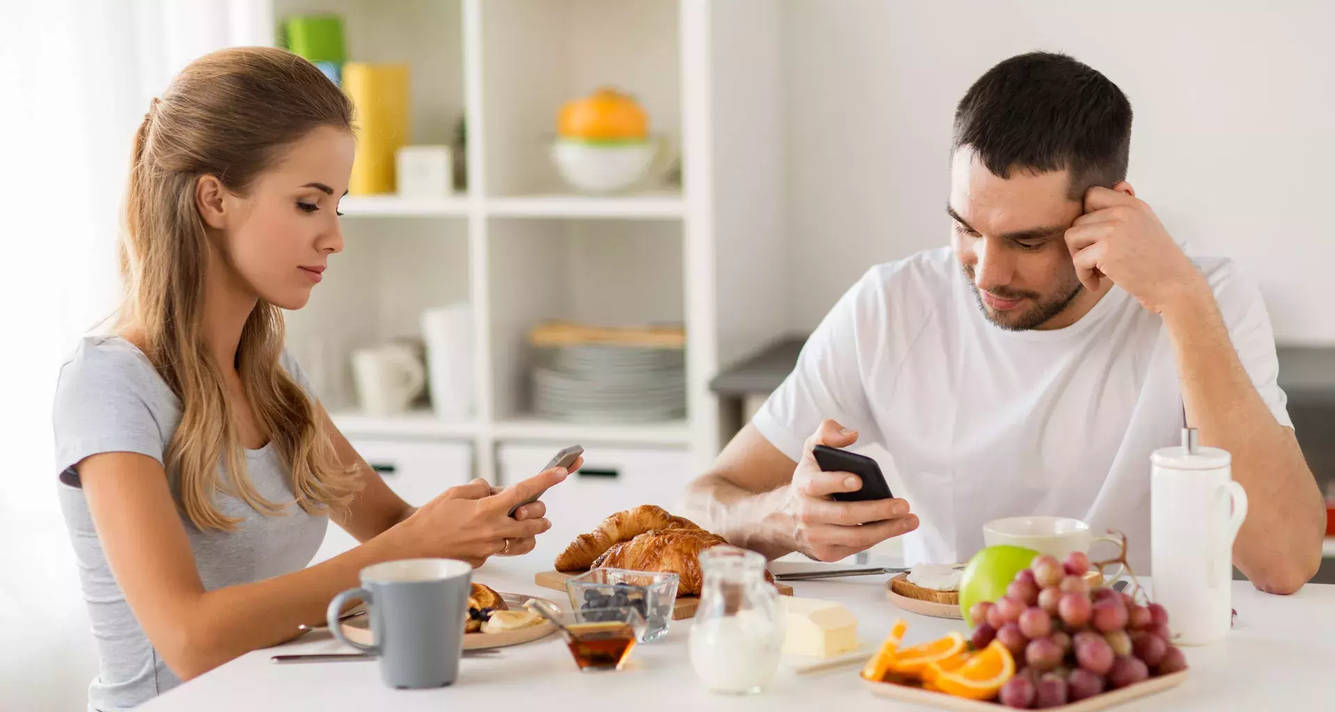 Dos personas comiendo mientras revisan sus dispositivos móviles.