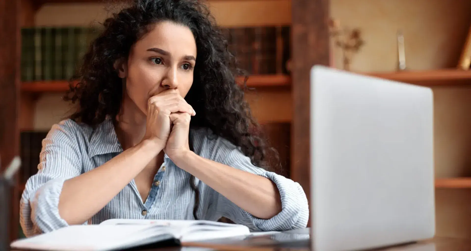 Mujer frente a laptop, con manos en la boca, signo de preocupación
