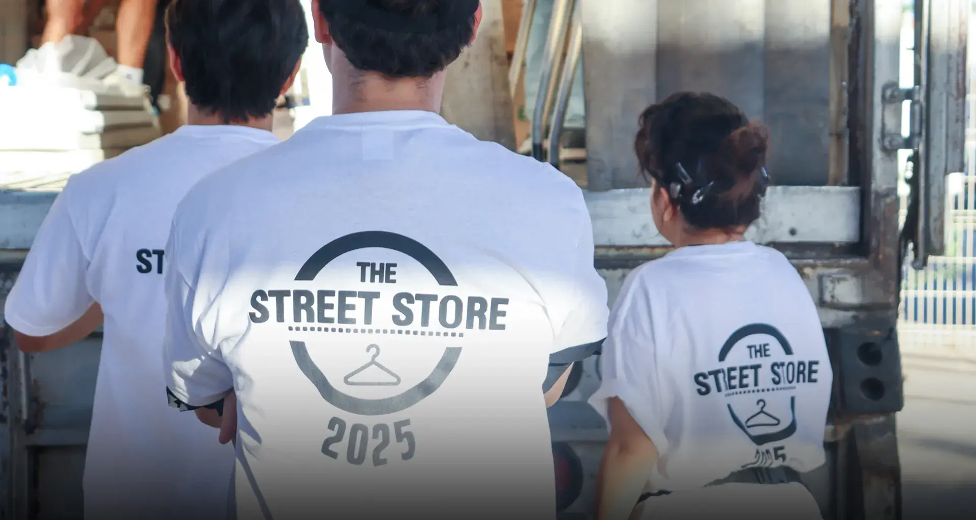 Vista de espaldas de tres voluntarios portando camisetas blancas con un logo que dice Street Store 2025