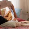 Mujer acostada en el piso de su casa leyendo un libro