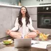 Joven con computadora, en posición de yoga y comida saludable alrededor, para representar el concepto de una rutina equilibrada