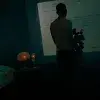 Vista de espalda del profesor Gonzalo Murúa sosteniendo una cámara de vídeo sobre un tripié, frente a una proyección de un cuento de su padre. 