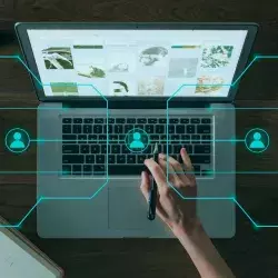 Laptop sobre escritorio, encima hay una imagen de red de contactos y una mano en el teclado.