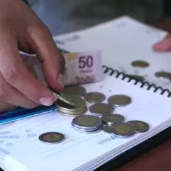 Persona cuenta dinero en escritorio con libreta y tarjetas bancarias