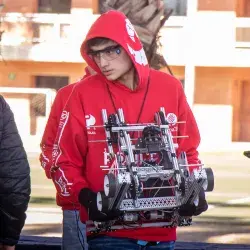 Estudiante joven lleva robot en sus manos en su participación en competencia de robótica