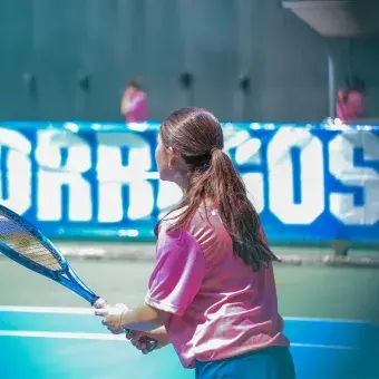 Alumna de espaldas sosteniendo raqueta de tenis. 